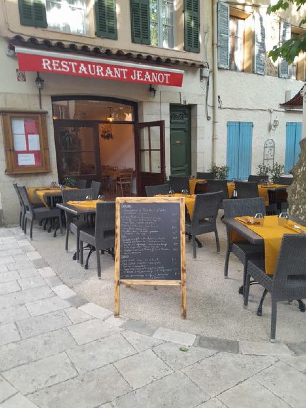 La façade du restaurant : auvent rouge « Restaurant Jeanot », ardoise du jour sur son chevalet et tables dressées en terrasse