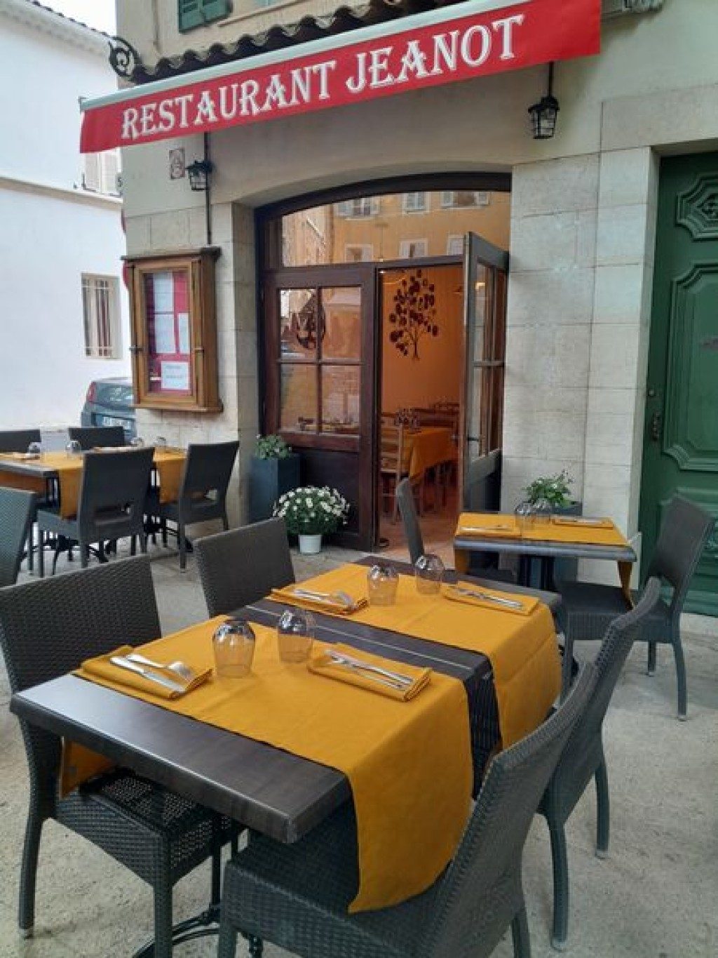 Une table dressée en terrasse, nappe moutarde, devant la porte vitrée du restaurant